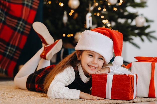 Una niña feliz con un sombrero de Santa Claus sonríe con regalos en sus manos.