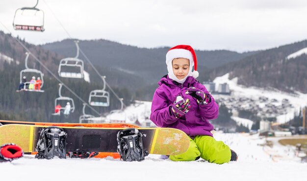 Niña feliz con sombrero de santa con tabla de snowboard