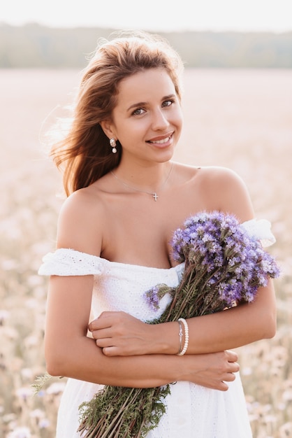 Niña feliz sonríe con un vestido blanco con un ramo de flores en el campo