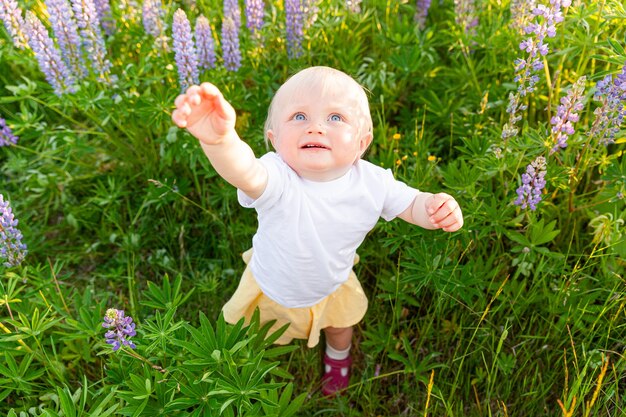 Niña feliz sonriendo al aire libre. Hermosa niña rubia joven descansando en el campo de verano con fondo verde de flores silvestres en flor