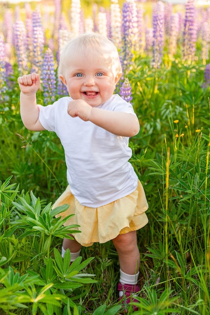 Niña feliz sonriendo al aire libre. Hermosa niña rubia joven descansando en el campo de verano con fondo verde de flores silvestres en flor