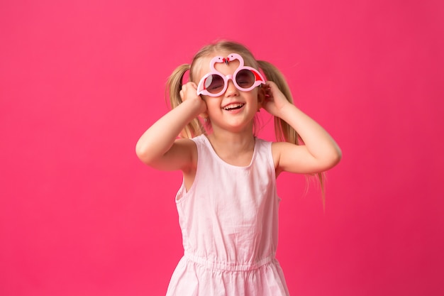 niña feliz sonriendo en gafas de sol sobre fondo rosa