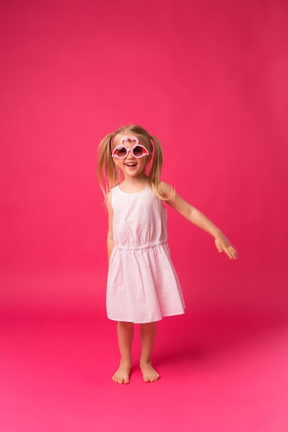 niña feliz sonriendo en gafas de sol sobre fondo rosa