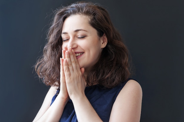 Niña feliz sonriendo. Mujer morena de risa positiva feliz joven del retrato de la belleza en la pared negra aislada. Mujer europea. Emoción humana positiva expresión facial lenguaje corporal