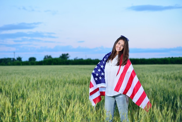 Niña feliz sonriente con la bandera americana sobre sus hombros