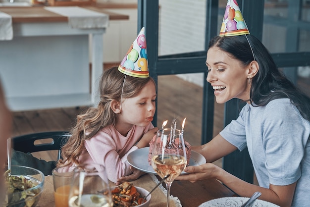 Niña feliz soplando velas en la torta de cumpleaños mientras cena con la familia