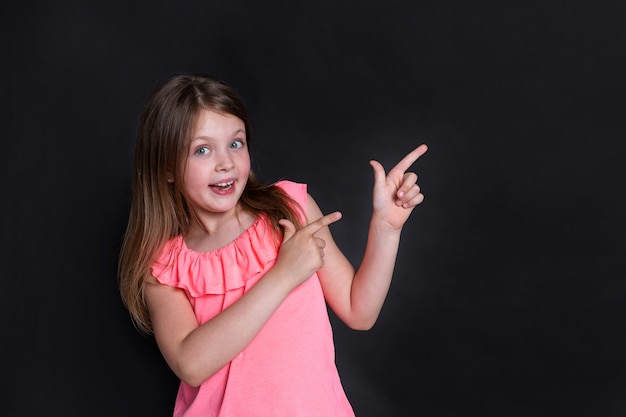 Una niña feliz sorprendida apunta a la derecha con las manos con los dedos hacia arriba