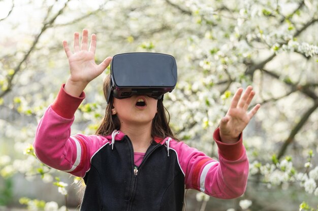 Niña feliz y sorprendida usando gafas de realidad virtual viendo películas o jugando videojuegos. Niño sorprendido alegre mirando en gafas VR y gesticulando