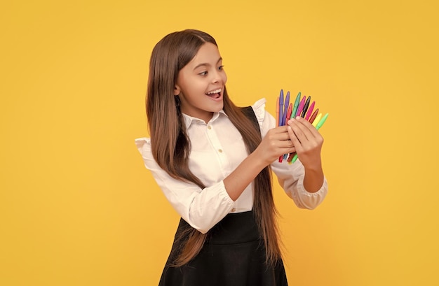 Niña feliz sostener rotuladores fondo amarillo papelería escolar