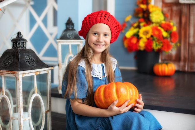 Niña feliz sosteniendo calabaza y sonriendo sentada en el porche de la casa y esperando truco o trato