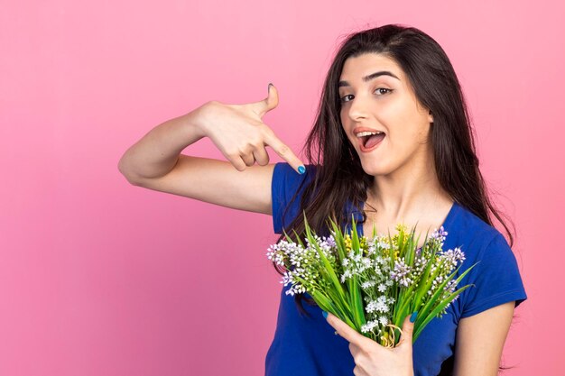 Niña feliz sosteniendo un ramo de flores y señalándolas con el dedo