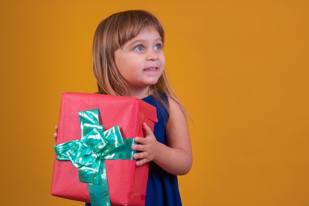 Foto niña feliz sosteniendo un regalo sobre fondo amarillo.