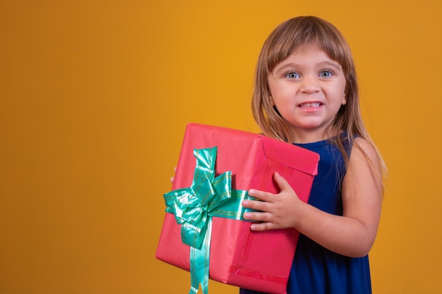 Niña feliz sosteniendo un regalo sobre fondo amarillo.