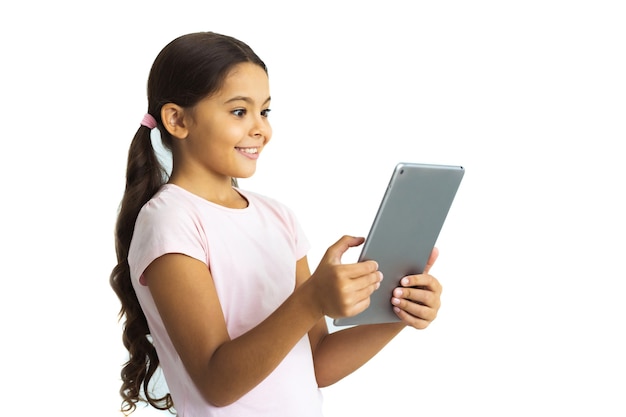 La niña feliz sosteniendo la tableta en el fondo de la pared blanca