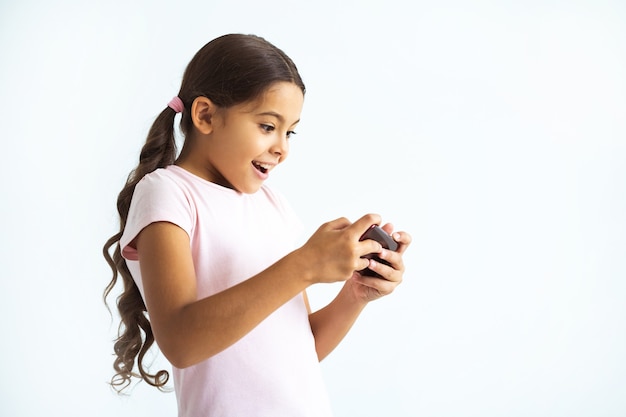 La niña feliz sosteniendo un teléfono en el fondo de la pared blanca