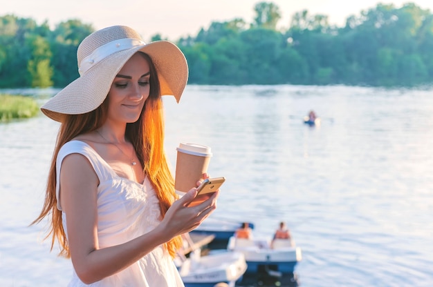 Niña feliz sosteniendo un teléfono inteligente con café en sus manos. En el contexto del agua de barcos y catamaranes.