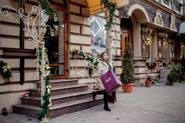 Niña feliz sostiene bolsas de papel con símbolo de venta en las tiendas con rebajas en Navidad