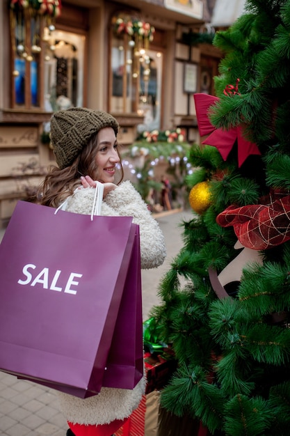 Niña feliz sostiene bolsas de papel con símbolo de venta en las tiendas con rebajas en Navidad