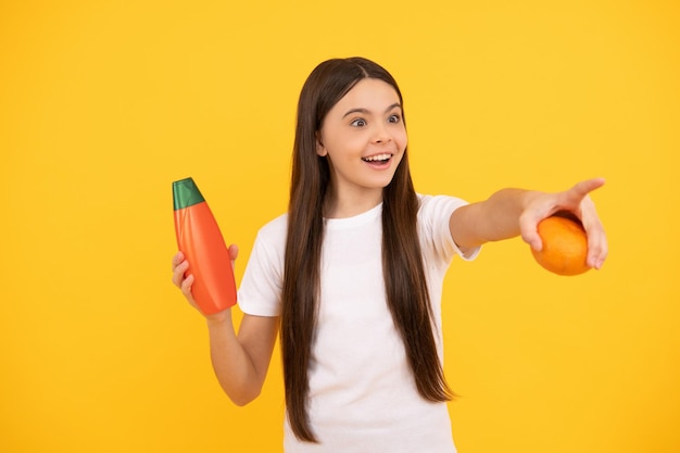 Niña feliz sostiene champú de toronja señalando con el dedo presentando productos cosméticos para adolescentes