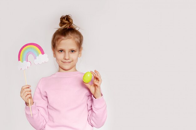 Una niña feliz sostiene un huevo de Pascua y un arcoiris en nubes de fieltro