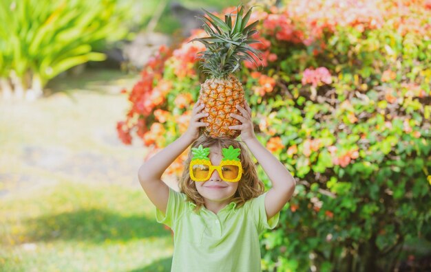 Una niña feliz sostiene una piña en la cabeza sobre un fondo natural de verano