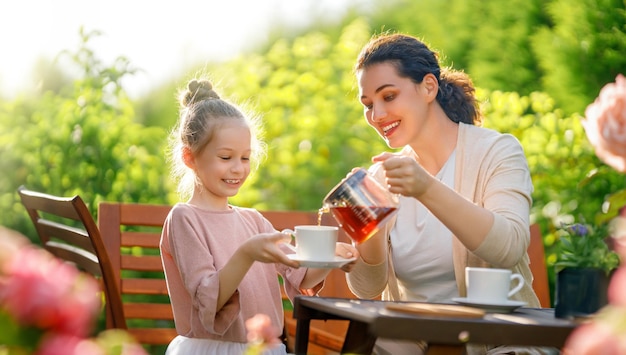 Niña feliz y su madre bebiendo té en una mañana de verano Familia sentada en el jardín