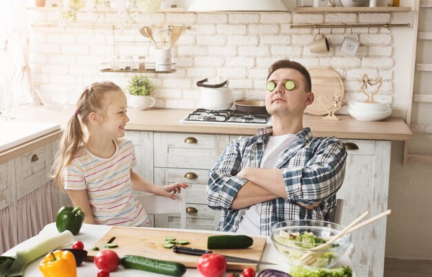 Niña feliz y su papá cocinando en la cocina de casa. Día del padre, vacaciones y concepto familiar.