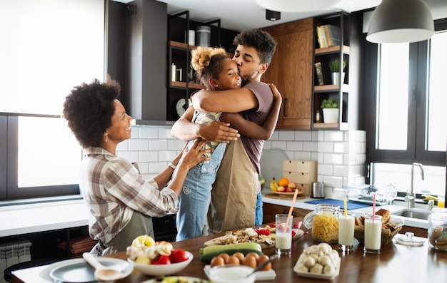 Foto niña feliz y sus hermosos padres están sonriendo mientras cocinan en la cocina de casa