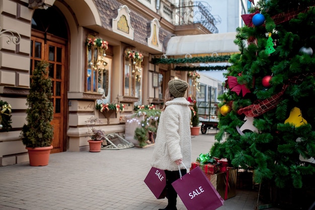 Niña feliz tiene bolsas de papel con símbolo de venta en las tiendas con rebajas en Navidad