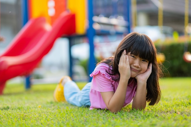 Niña feliz tirada en el patio de juegos de hierba