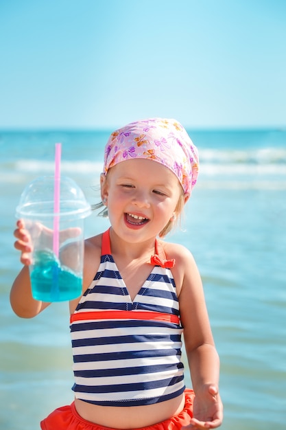 Niña feliz en traje de baño con cóctel azul en la playa. Verano. Vacaciones. Mar. Oceano.