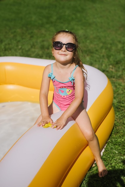 Niña feliz en traje de baño jugando en la piscina inflable en un día soleado