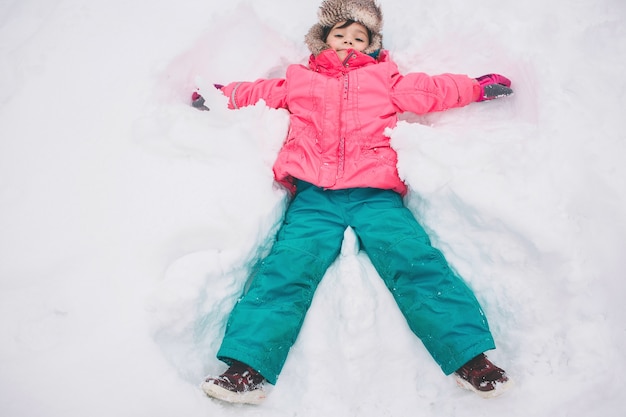 Niña feliz tumbado en la nieve.