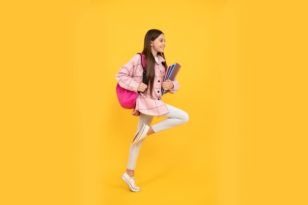 Niña feliz usa camisa rosa a cuadros corriendo con mochila escolar y cuadernos, date prisa.