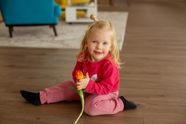 una niña feliz vestida de casa está sentada en el suelo con un tulipán en las manos