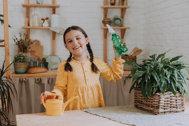 una niña feliz con un vestido de algodón amarillo está regando flores en la dacha. terraza de madera