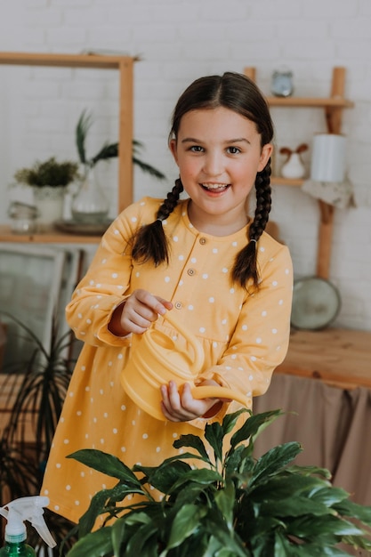 una niña feliz con un vestido de algodón amarillo está regando flores en la dacha. terraza de madera