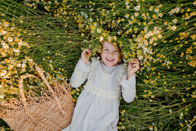 Niña feliz con un vestido de algodón se encuentra en un campo de margaritas en el verano al atardecer. risas, vista desde arriba