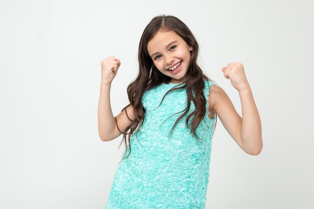 Niña feliz con un vestido azul disfruta de las ganancias en una pared blanca del estudio