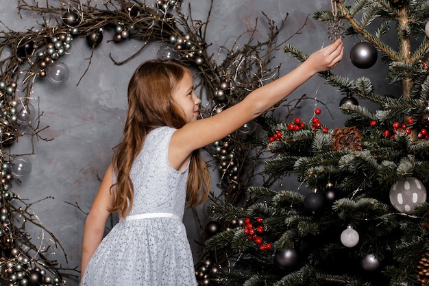 Niña feliz en vestido azul que adorna el árbol de Navidad.