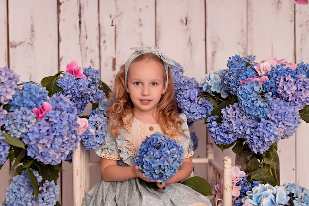 Niña feliz con un vestido en el estudio sobre un fondo blanco con flores de hortensias rosas y azules