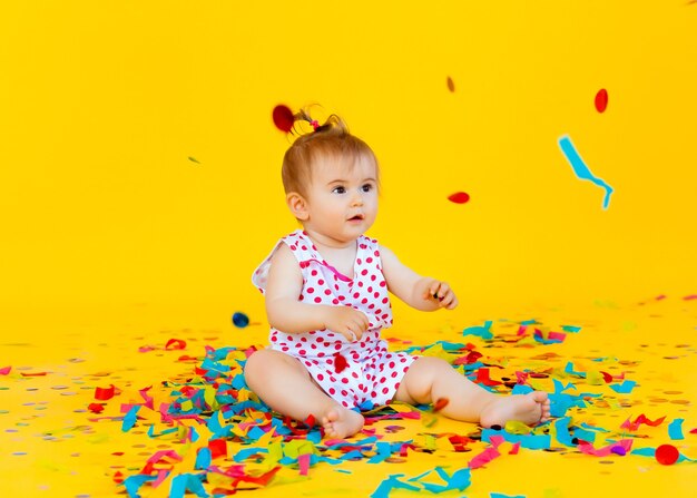 Niña feliz con un vestido de guisantes atrapa confeti sobre un fondo amarillo. lugar para el texto