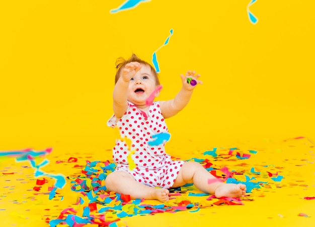 Niña feliz con un vestido de guisantes atrapa confeti sobre un fondo amarillo. lugar para el texto