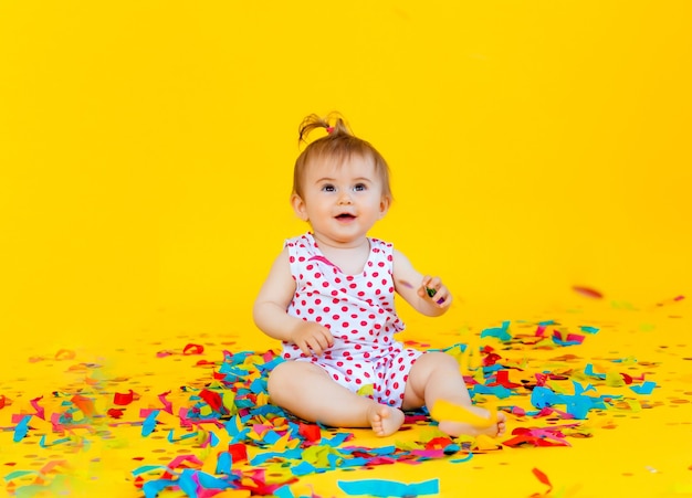 Niña feliz con un vestido de guisantes atrapa confeti sobre un fondo amarillo. lugar para el texto