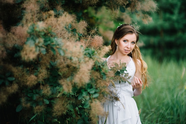 Niña feliz con un vestido largo turquesa en un parque verde sobre un fondo de hierbas, árboles y rosales