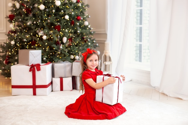 Niña feliz en vestido rojo con regalo de Navidad