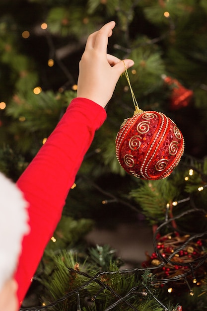 Niña festiva que cuelga una decoración de la Navidad