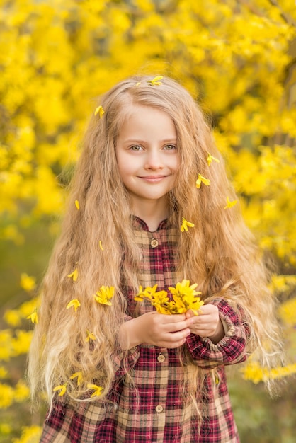 Niña con flores amarillas en sus manos. Un niño sobre un fondo de flores amarillas. Retrato de primavera de un niño