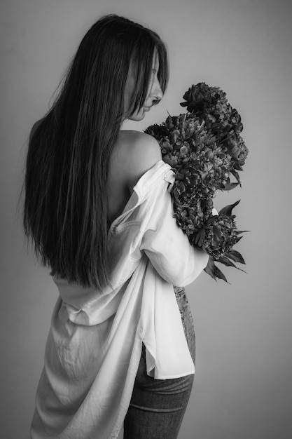 Una niña con flores en una camisa blanca cerca de la pared.