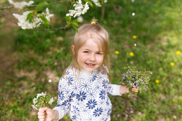 Niña con flores de primavera sobre césped verde en el jardín.